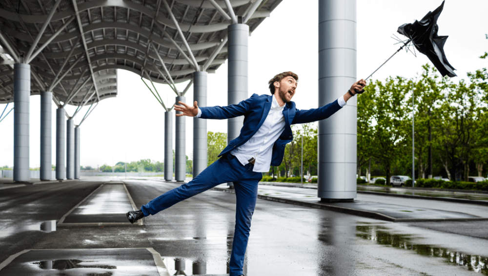 A man is affected by the wind, and his umbrella is about to fly away.