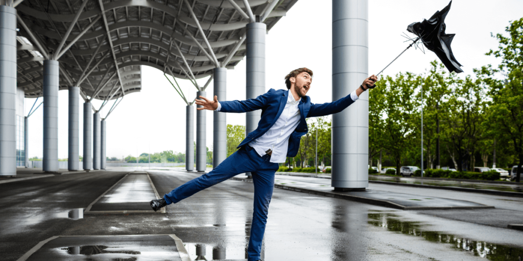 A man is affected by the wind, and his umbrella is about to fly away.