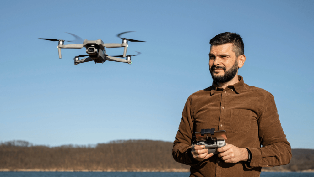 A man wearing a brown shirt focused on flying a drone outdoors.