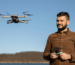 A man wearing a brown shirt focused on flying a drone outdoors.